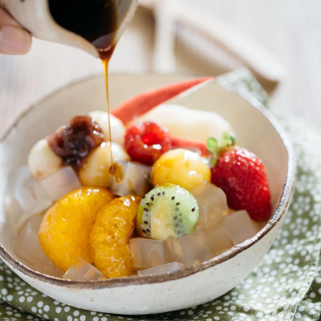 Kuromitsu syrup is pouring over Anmitsu in a small bowl