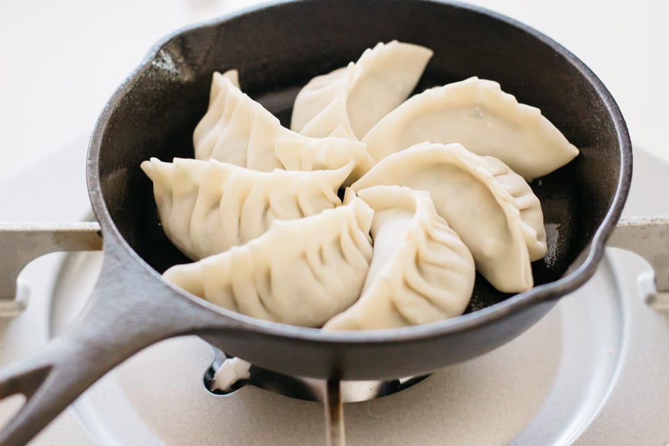 seven pieces of gyoza being fried in a small cast iron skillet