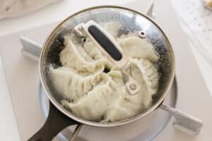 6 gyoza being fried in a cast iron skillet with a glass lid on