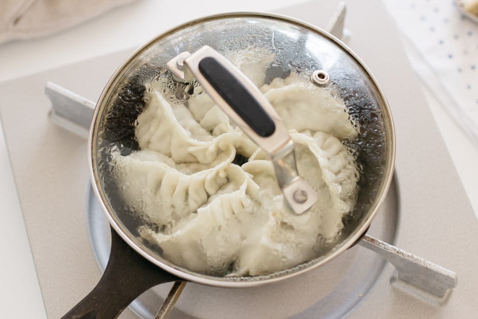 seven dumplings being steam fried in a cast iron skillet with a lid on