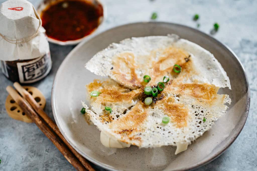 Gyoza with lattice served on a round plate with a bowl of dipping sauce in background