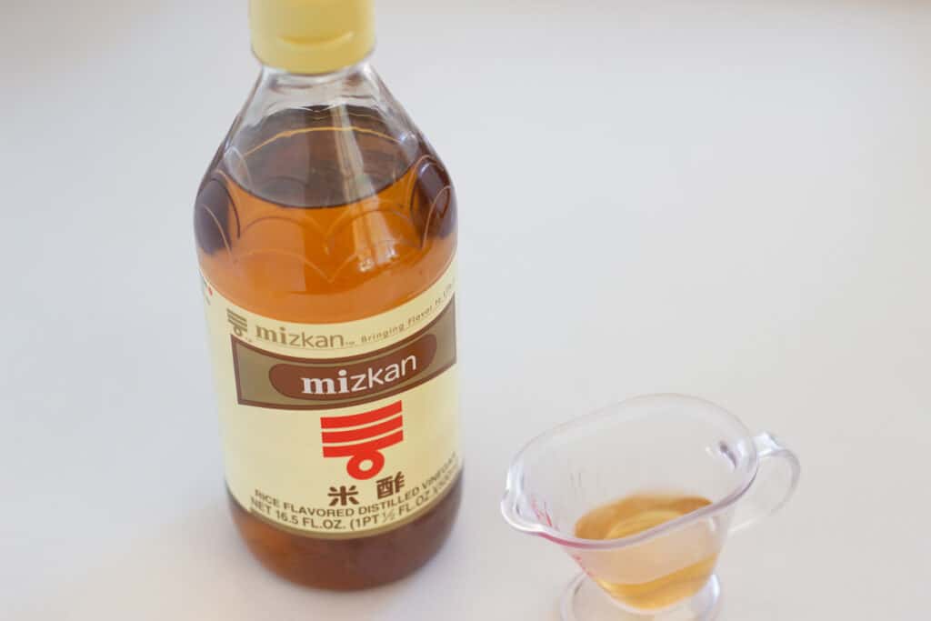 A mizkan brand rice vinegar bottle and the vinegar in a small measurement jug 