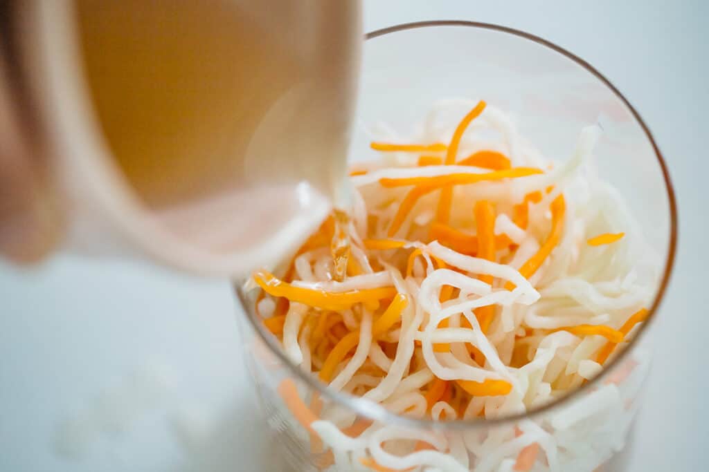 daikon and carrot in a large mixing bowl and pouring over a bowl of vinaigrette 