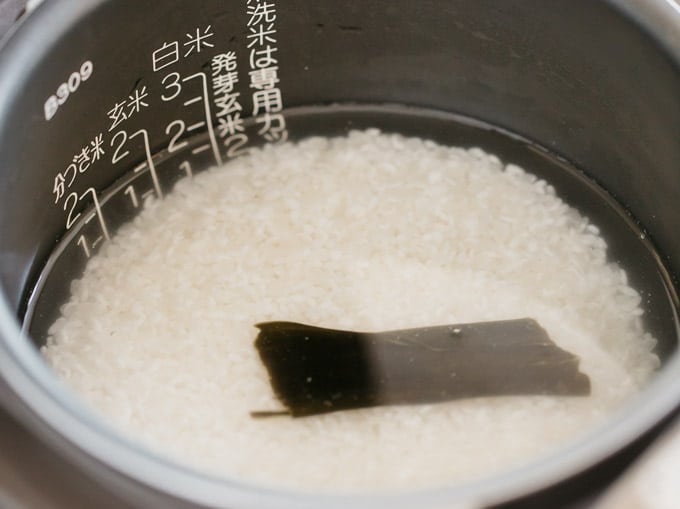 rinsed rice with a strip of kelp in a rice cooker bowl