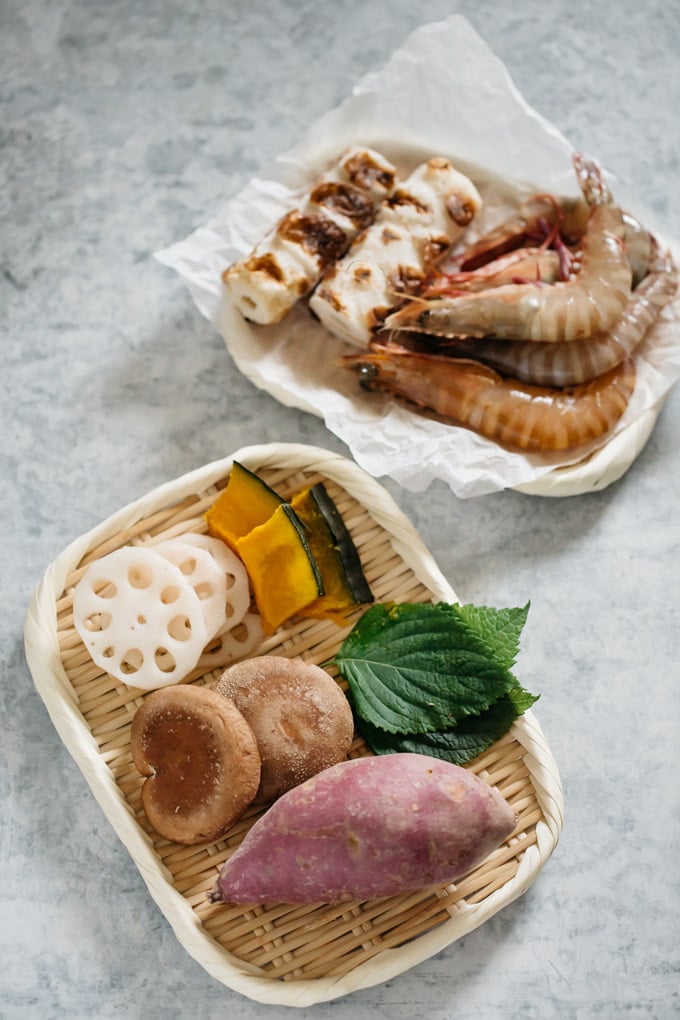 ingredients-sweet potato, shiitake mushrooms, shiso leaves, renkon, and kabocha slices, prawns, and chikuwa fish cake on bamboo trays 