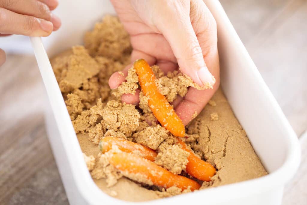 a hand digging out carrots pickled in rice bran pickling bed. 