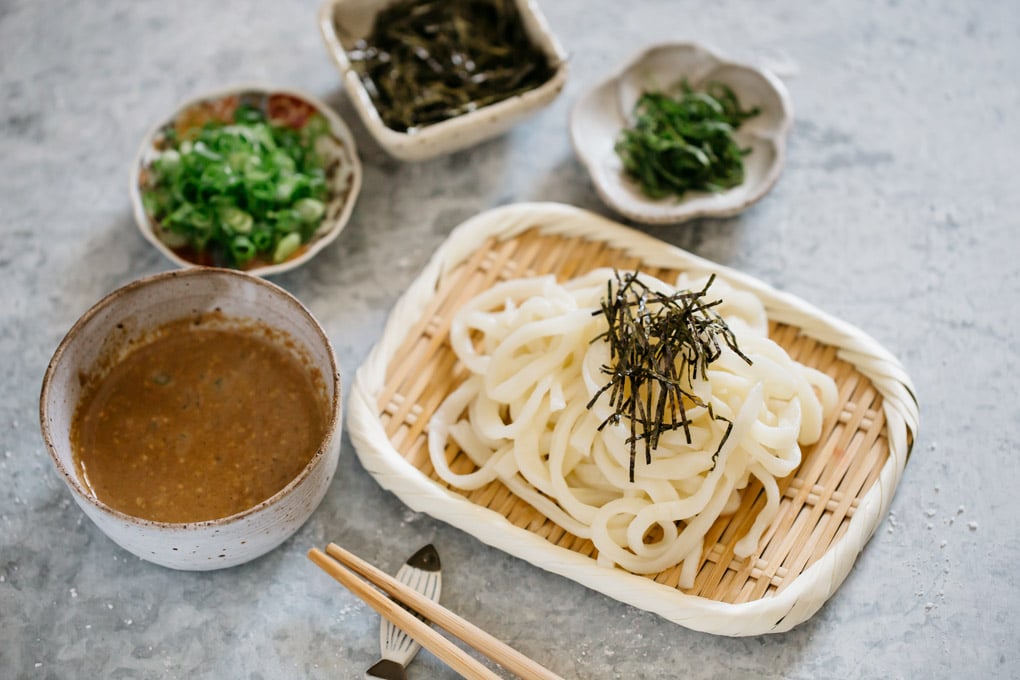 Udon noodles served on a bamboo tray with a small bowl of dipping sauce and yakumi