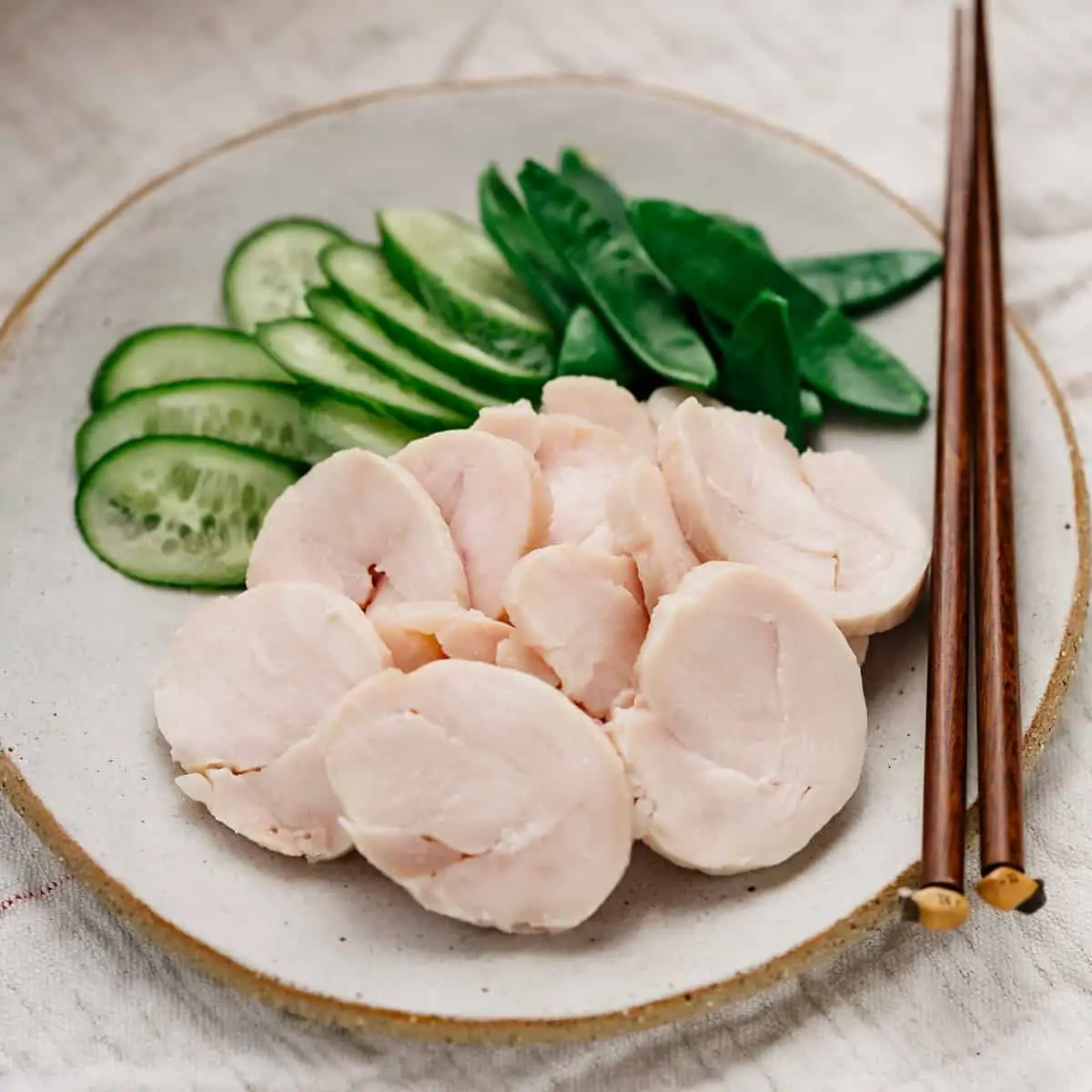 slices of chicken ham and cucumber and snap peas on a round plate with a pair of chopsticks