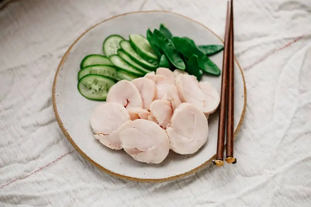 Sliced chicken ham with cucumber and snap peas on a round plate