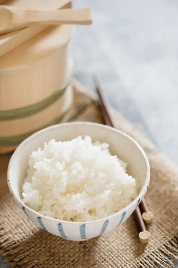 Japanese plain steamed rice in a Japanese rice bowl with a pair of chopstick and wooden container of rice