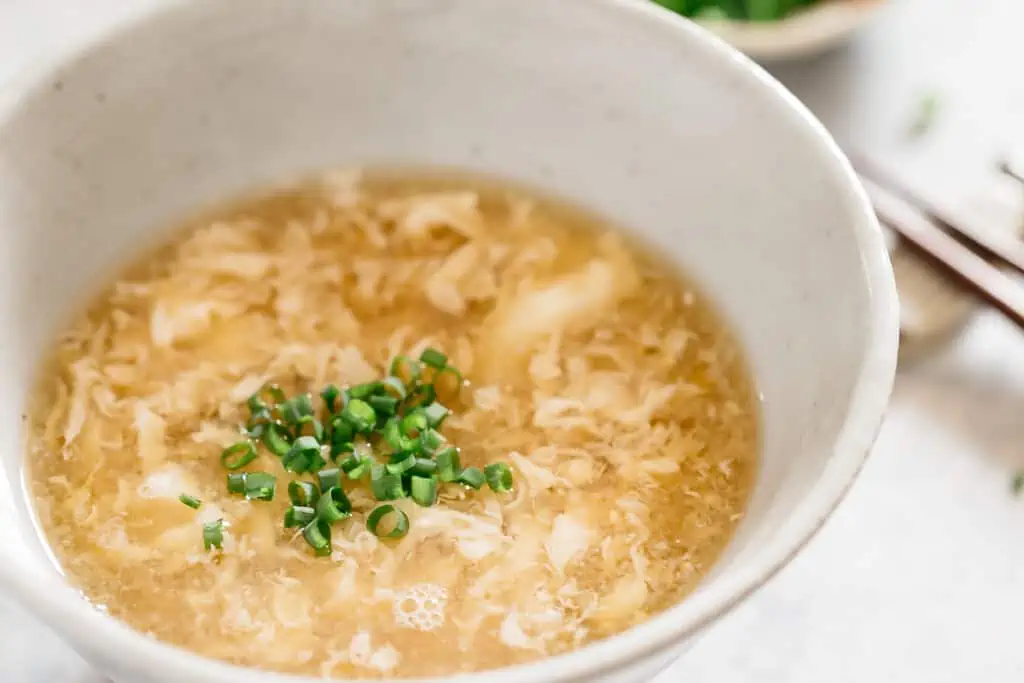 egg drop soup garnished with chopped scallions served in a serving bowl
