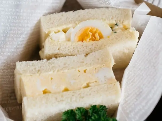 an egg omelette sandwich and an egg salad sandwich in a cardboard take away container