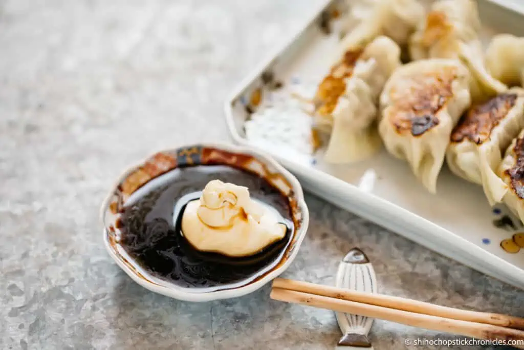 soy sauce and Japanese mayonnaise in a small bowl and gyoza dumplings on a plate in background