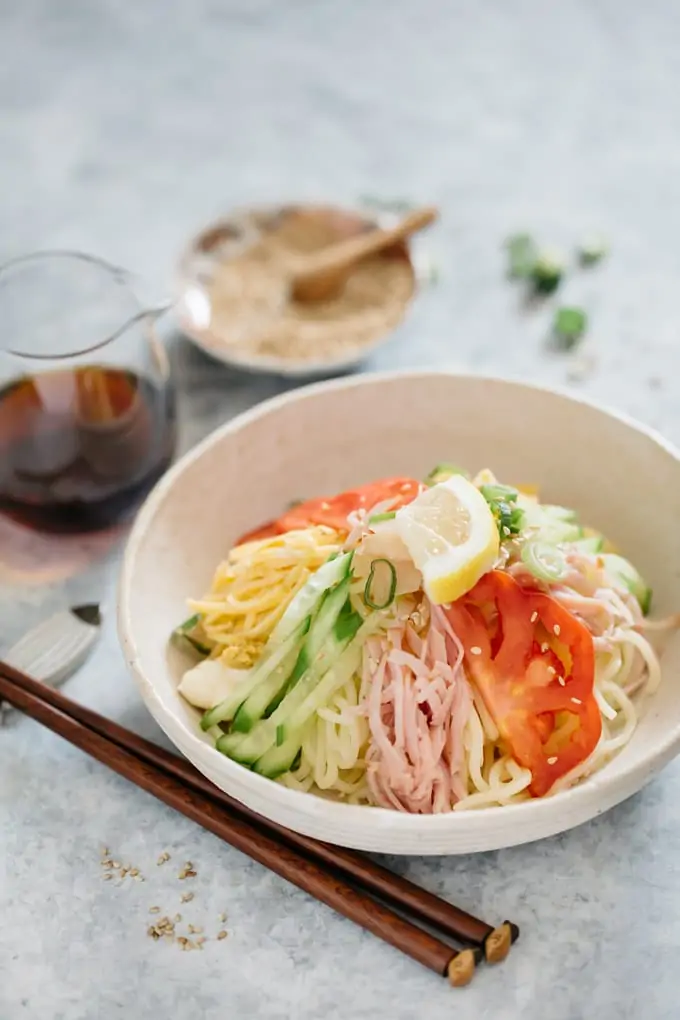 Hiyashi chuka served in a white shallow bowl and a small jar of dipping sauce and a pair of chopstick