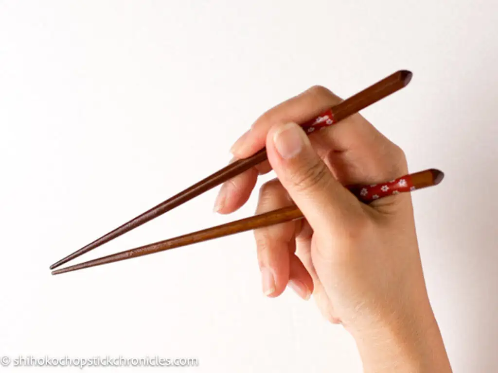 the bottom chopsticks rest on the base of thumb and index finger and moving the top chopsticks with pencil grip