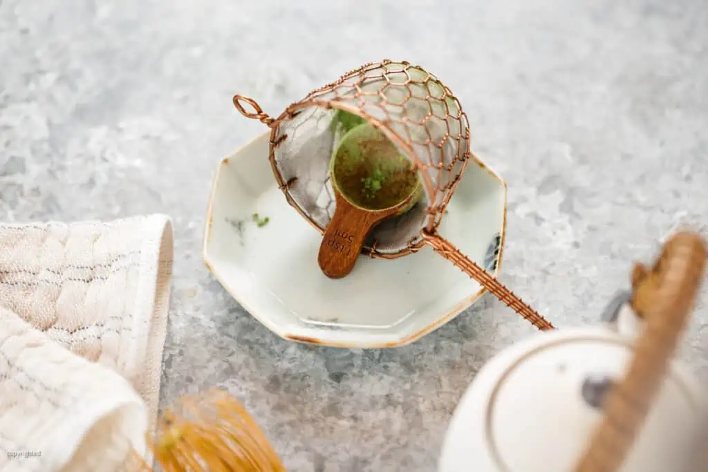matcha tea spoon and shifter on a small plate, a bamboo whisk and a teapot