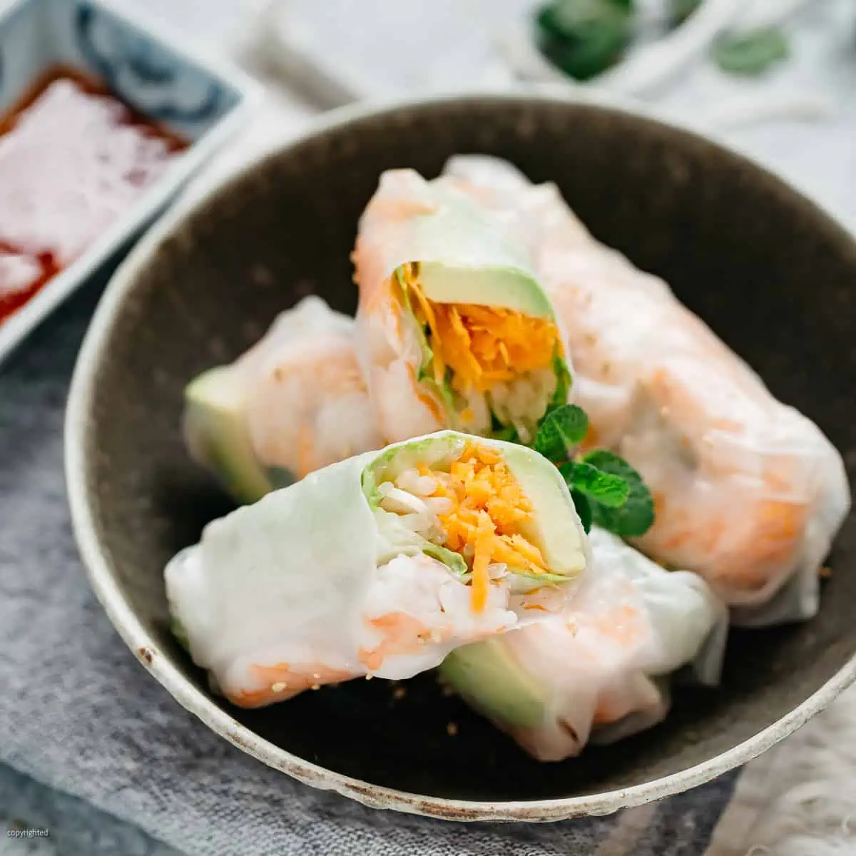 two japanese rice paper rolls and one in half on a dark shallow plate