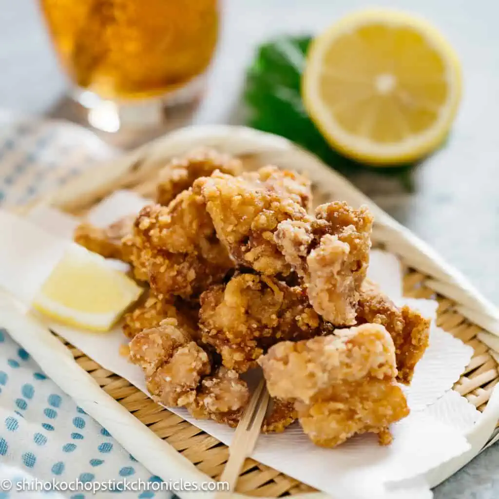 karaage chicken served on a bamboo tray with a glass of drink and half cut lemon