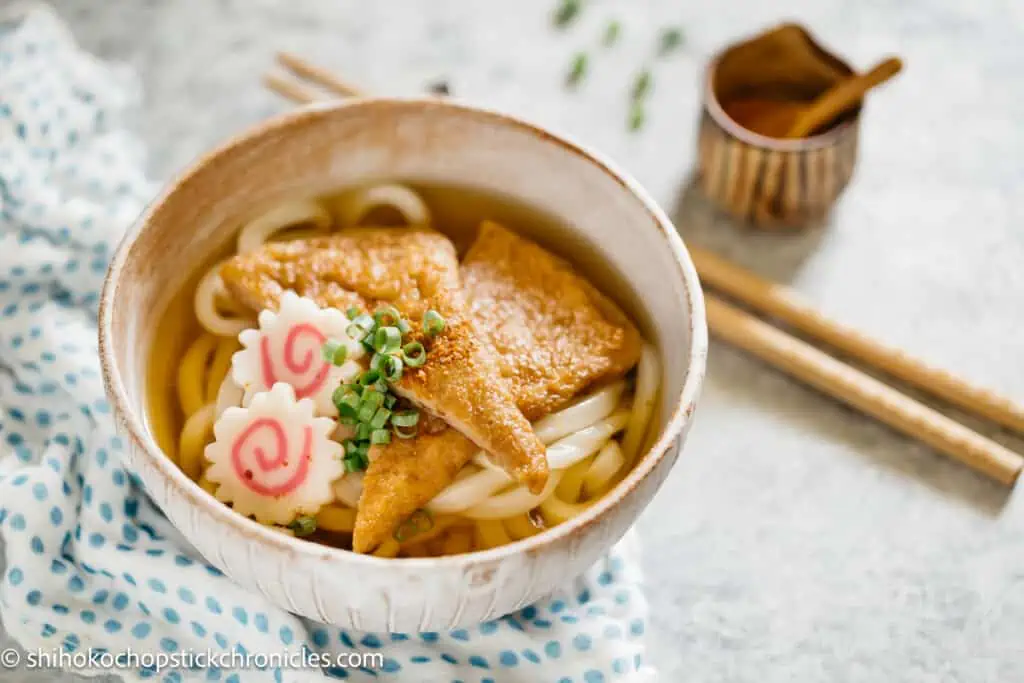 kitsune udon served in a noodles bowl with two naruto in it and a pair of chopsticks