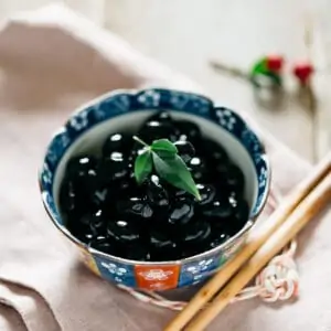 Sweetened black soybeans served in a small bowl with a pair of chopsticks