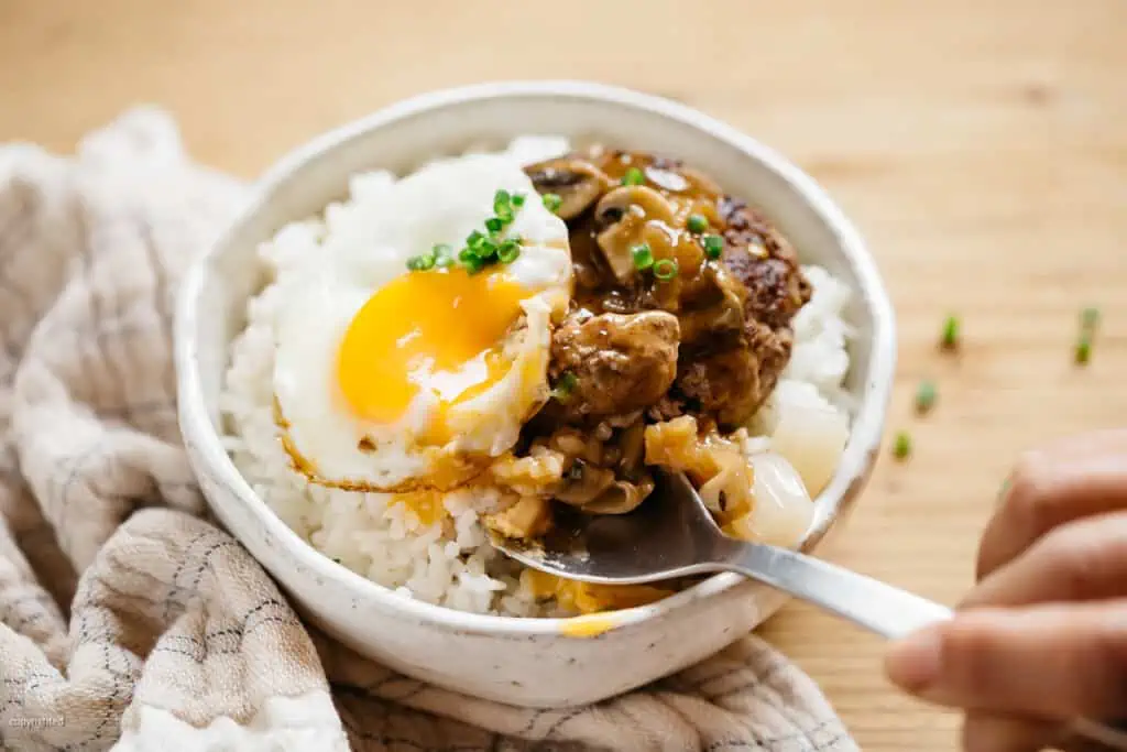 Loco moco donburi is served in a rice bowl with a spoon scooping some
