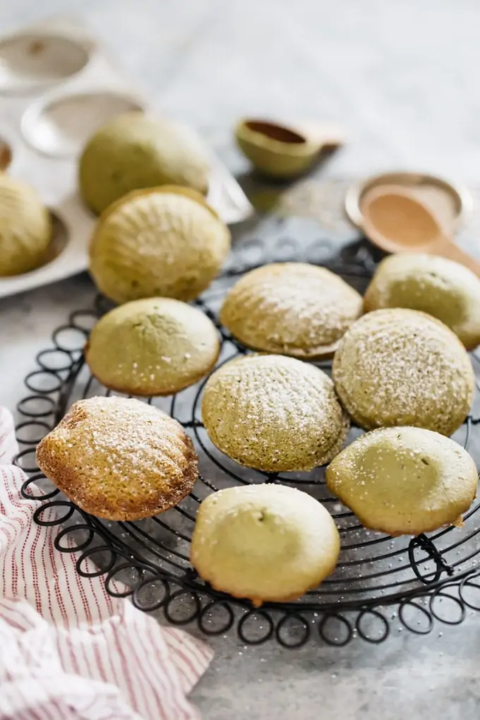 Freshly baked matcha madeleines cooling on a black round wire rack