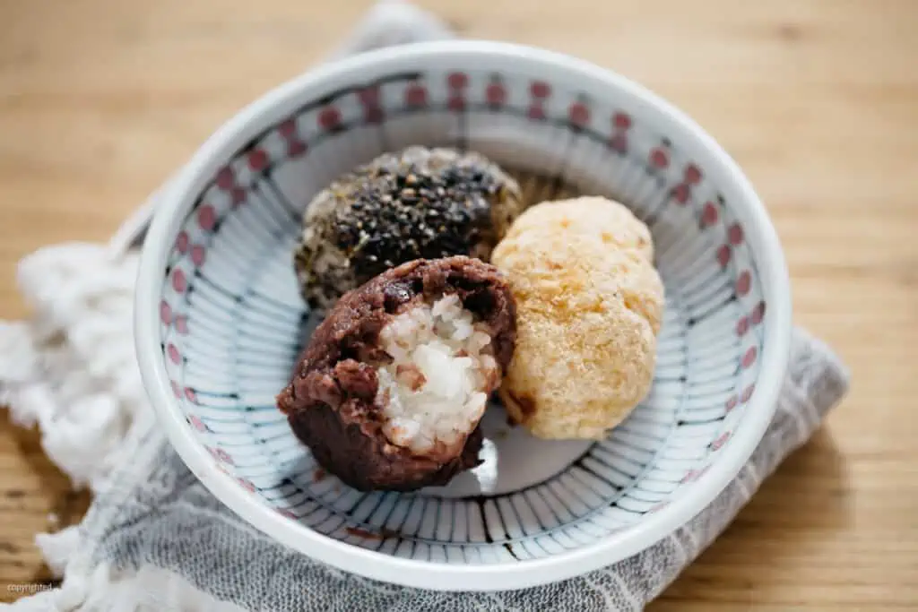 three ohagi, with anko, kinako soybean powder, and black sesame seeds on a round plate