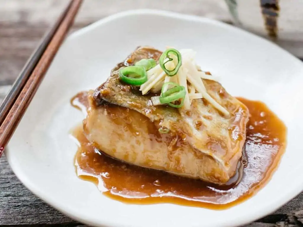 mackerel simmered in sweet miso, soy sauce and mirin sesrved on a white plate with finely chopped ginger