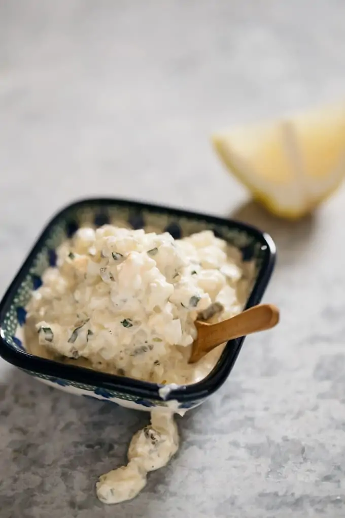 Tartar sauce in a small square bowl with a piece of lemon in background