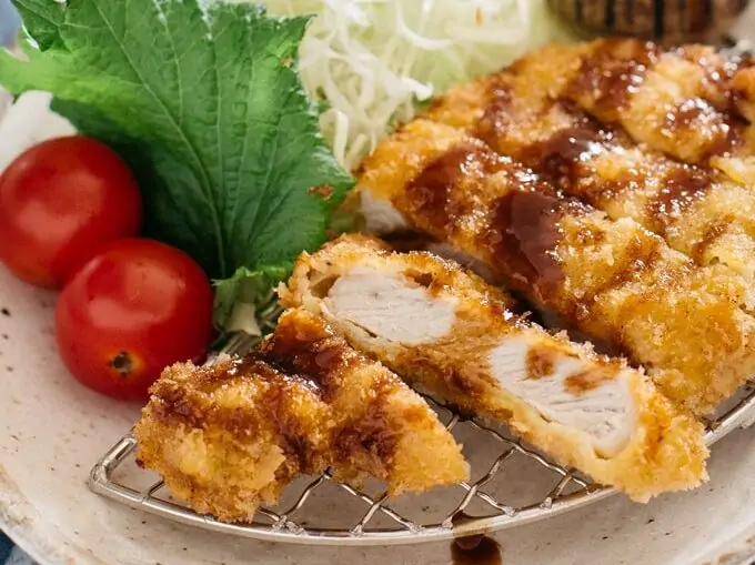Tonkatsu served on an oval plate with shredded cabbage and tomatoes