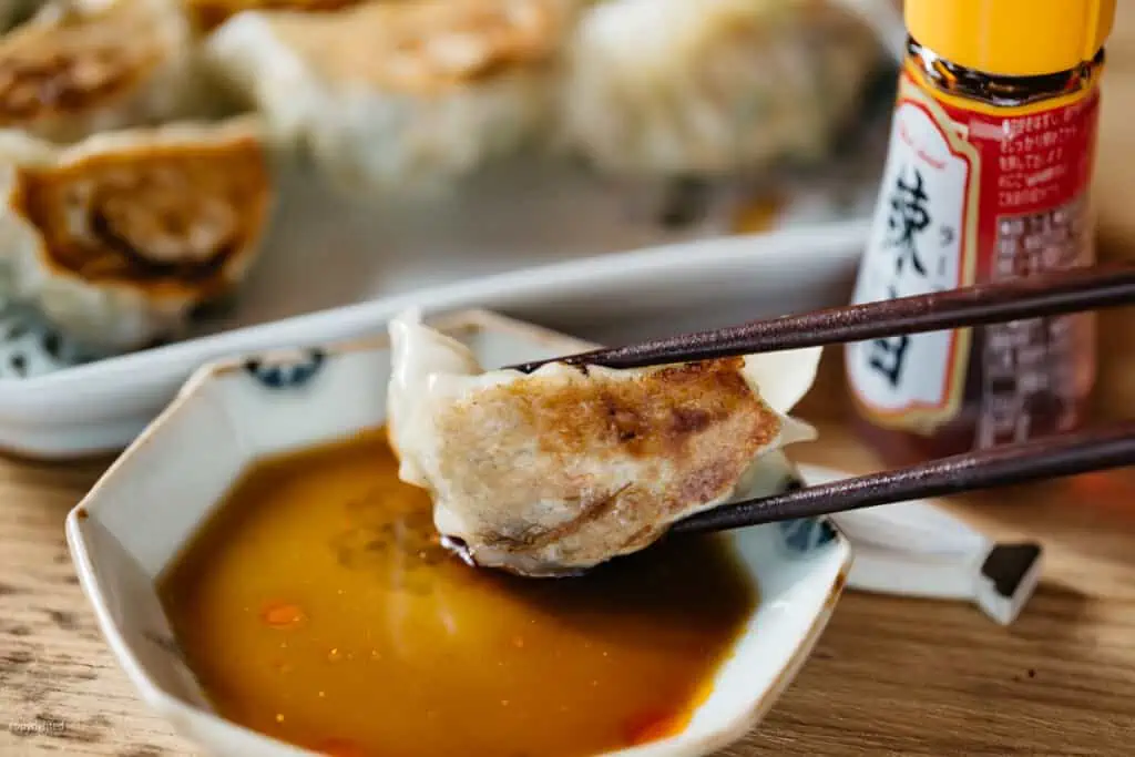 one gyoza with a pair of chopsticks dipped in a small bowl of gyoza sauce