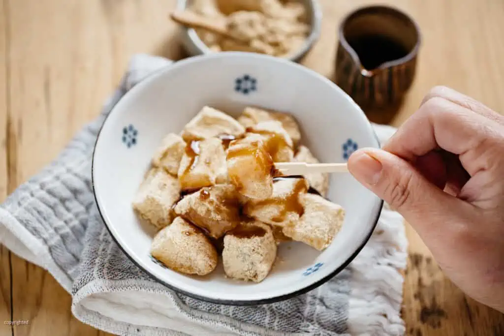 warabi mochi served in a small bowl with a small bowl of kinako soybean powder and kuromitsu in a small pottery jar